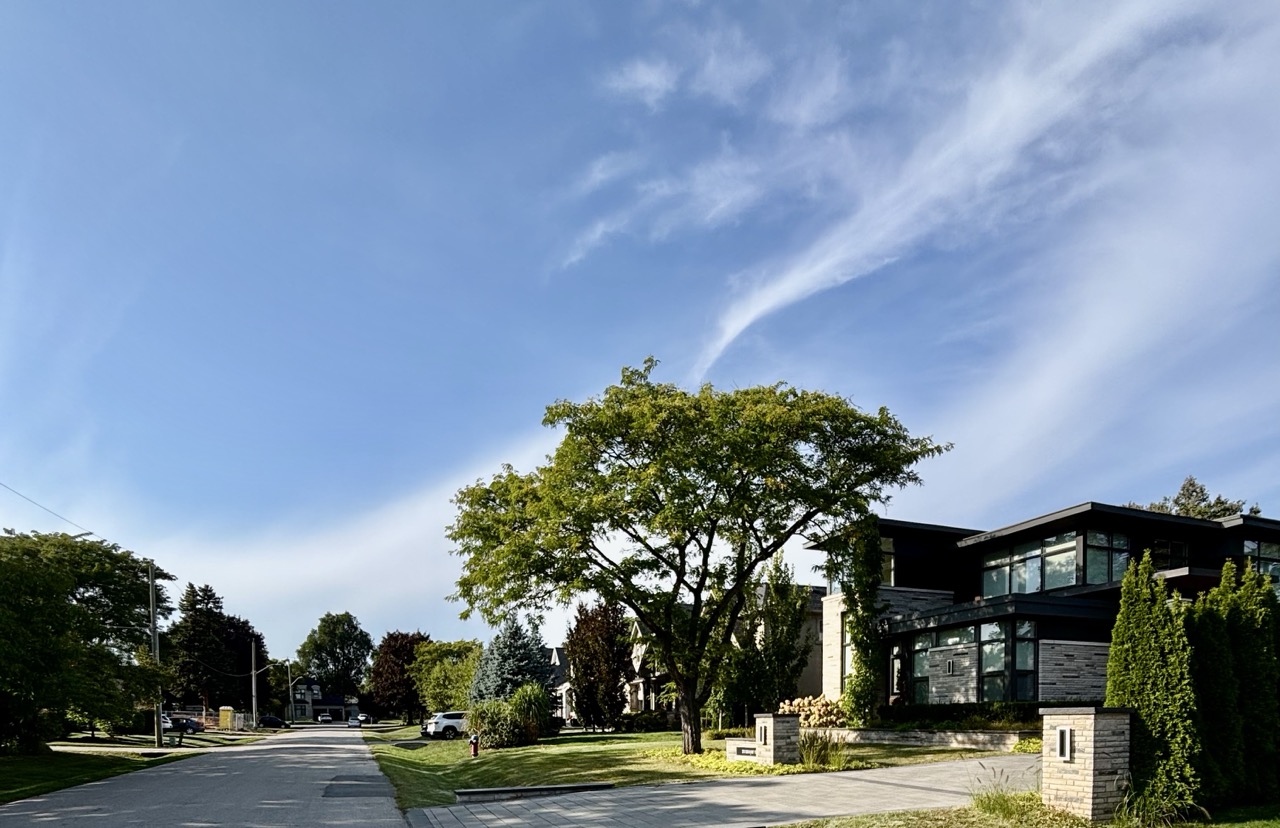 Wide gravel walking path on the Donovan Bailey Trail in Bronte, Oakville, lined with lush green, and early autumn Trees under a bright blue sky with scattered clouds.